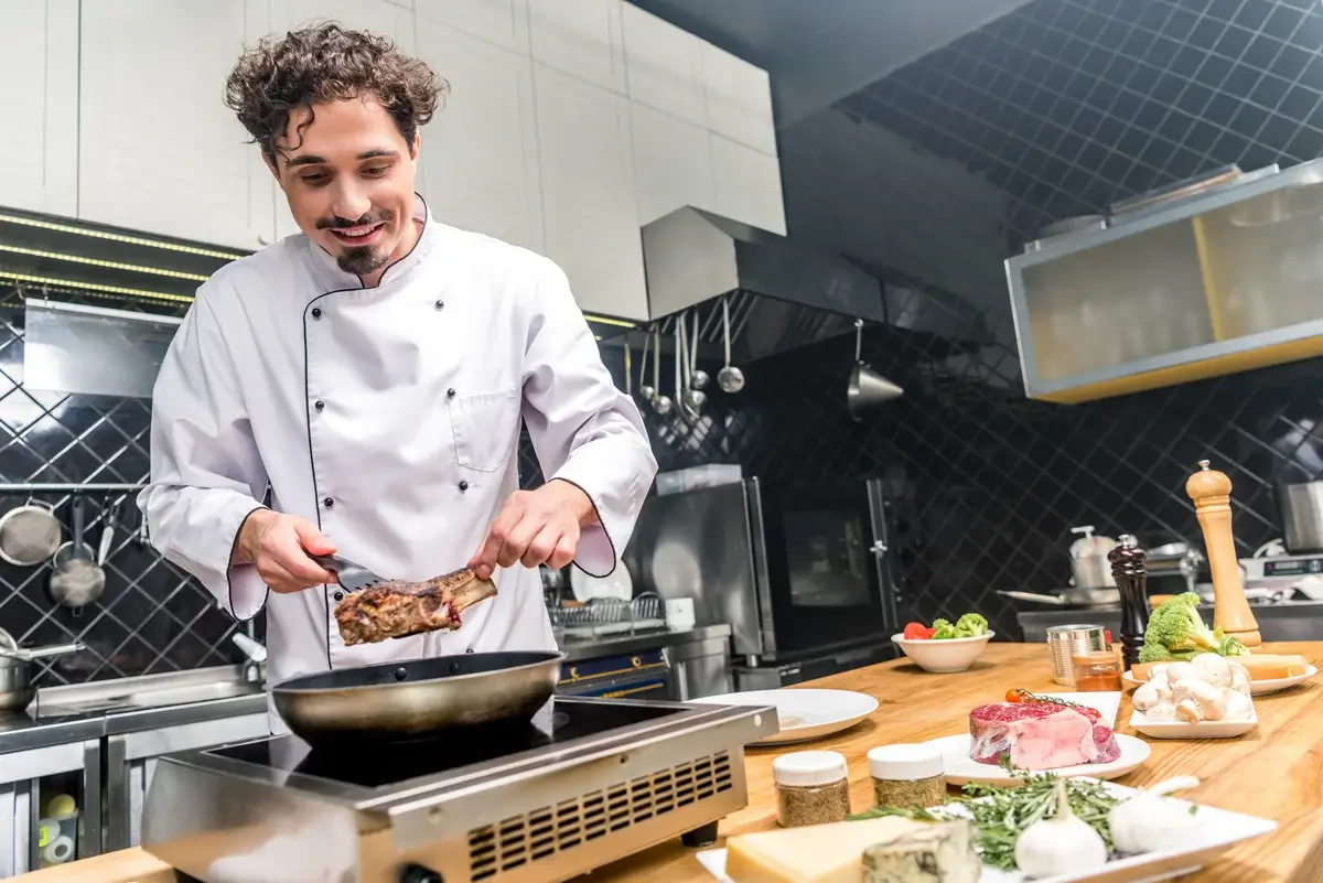 smiling-chef-frying-meat-in-restaurant-kitchen