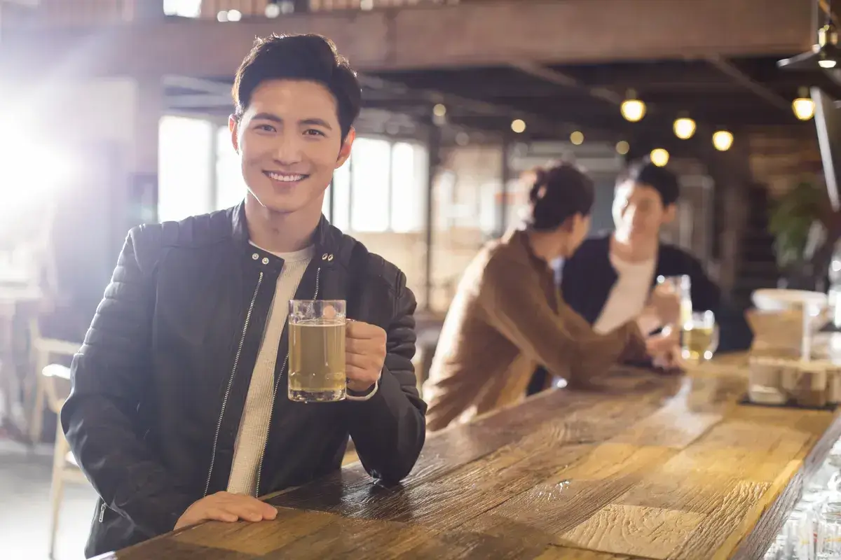 happy-young-chinese-man-drinking-beer-in-bar
